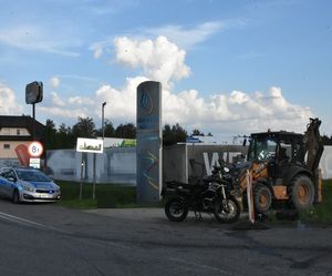 motocykl oraz koparka poza drogą. nieopodal stoi radiowóz