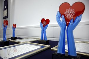 cztery statuetki ustawione na biurku przedstawiające niebieskie przedramiona i dłonie trzymające czerwone serce. Obok nich lezące listy gratulacyjne