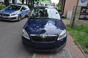 samochód stoi częściowo na chodniku. Za nim po drugiej stronie ulicy radiowóz