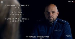 siedzący policjant. Po lewej stronie wypisane numery alarmowe