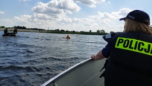 policjantka na łodzi. Na wodzie widoczny ponton i siedzący w nim funkcjonariusze SG. W wodzie strażacy