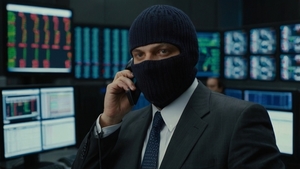 mężczyzna siedzący z kominiarką na głowie rozmawia przez telefon komórkowy. Za nim rozmyte monitory