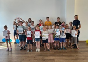 policjantka podczas spotkania z dziećmi. Zdjęcie grupowe. Dzieci trzymają w rękach własnoręcznie wykonane materiały