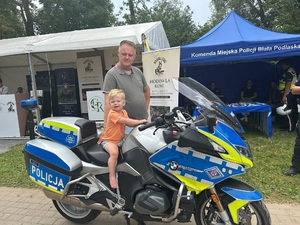 dziecko siedzące na motocyklu. Obok opiekun