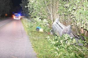 uszkodzony samochód leżący w rowie. Za nim  widoczny stojący na drodze radiowóz