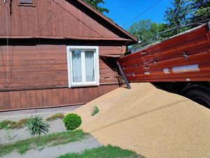 uszkodzony dom, obok fragment przyczepy i wysypane zboże
