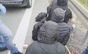 migranci siedzący tyłem na ulicy z kapturami założonymi na głowy