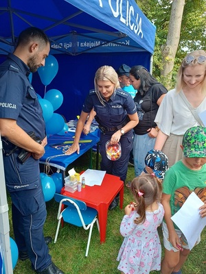 policjanci przy stoisku. Policjantka częstuje dzieci cukierkami