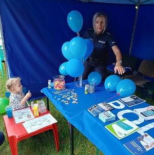 policjantka w policyjnym namiocie . Obok dziecko przy stoliku z kolorowankami