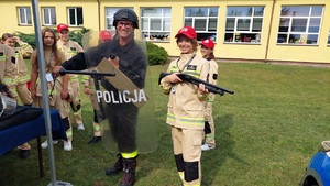 osoby odwiedzające stoisko przymierzają wyposażenie. Strażak trzyma tarcze i pałkę obok niego dziewczynka