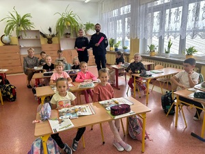 policjanci podczas spotkania z dziećmi. Uczniowie siedzą w ławkach, natomiast policjanci trzymają w dłoniach opaski odblaskowe