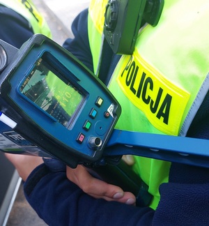 policjant trzyma rejestrator. Na rejestratorze widoczny pomiar