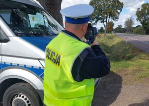 policjant ruchu drogowego stoi przy radiowozie. W oddali widoczny ciągnik