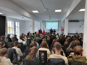 policjanci stoją przy stole prezydialnym. Przed nimi uczestnicy debaty