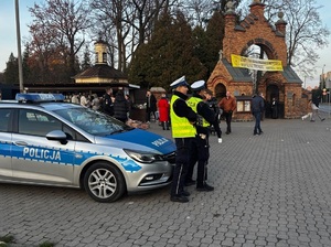 policjanci wydziału ruchu drogowego stoją przy radiowozie w rejonie cmentarza