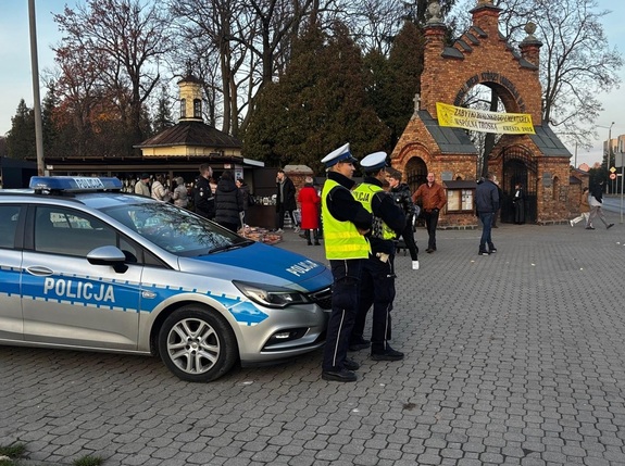 policjanci wydziału ruchu drogowego stoją przy radiowozie w rejonie cmentarza