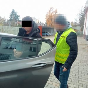 nieumundurowany policjant wprowadza zatrzymanego do radiowozu