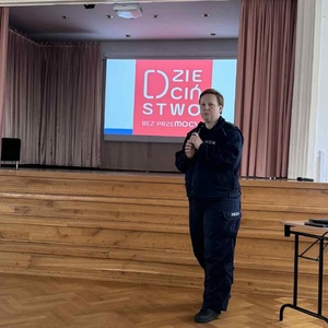 policjantka podczas prelekcji, za nią widoczny baner z napisem dzieciństwo bez przemocy