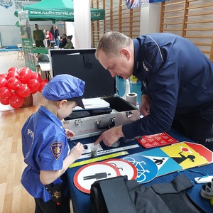 policjant na stoisku pokazuje dzieciom jak zabezpieczać odbitki linii papilarnych