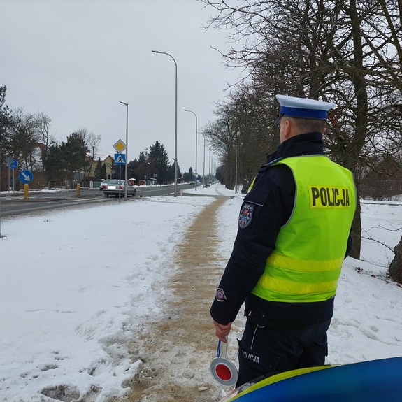 policjant ruchu drogowego stoi przy radiowozie w rejonie przejścia  dla pieszych