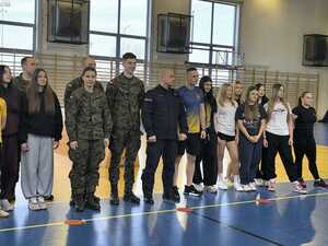 Funkcjonariusz Policji z uczniami i Wosjkiem stojący w sali gimnastycznej