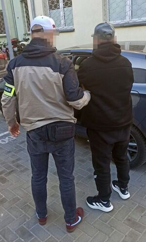 Nieumundurowany policjant prowadzi zatrzymanego do radiowozu