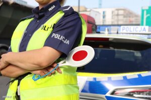 Umundurowana policjantka z tarczą do zatrzymywania pojazdów stojąca obok radiowozu
