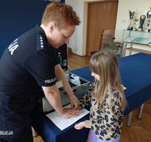policjantka pokazuje dziecku sposób zabezpieczania odbitek linii papilarnych