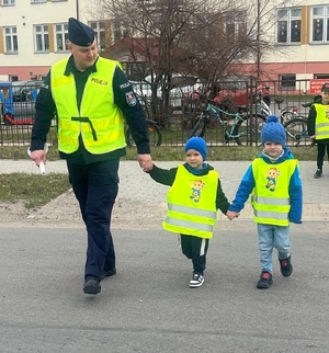 policjant przechodzi z dziećmi przez przejście dla pieszych.