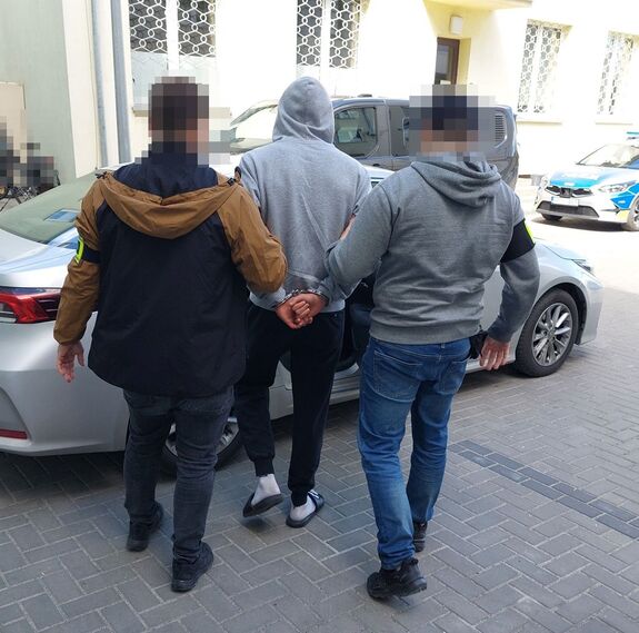 nieumundurowani policjanci prowadzą zatrzymanego mężczyznę do smochodu