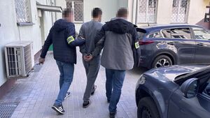 dwóch nieumundurowanych policjantów prowadzi zatrzymanego męzczyznę