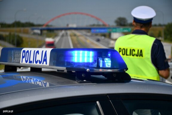 policjant ruchu drogowego stojący obok oznakowanego radiowozu