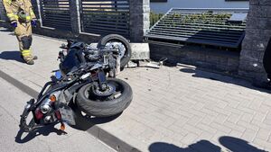 motor leżący częściowo na jezdni, a częściowo na chodniku, obok uszkodzonego ogrodzenia posesji
