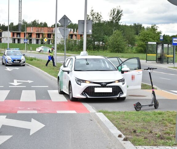 samochód osobowy oraz hulajnoga. Za nim radiowóz i funkcjonariusz wykonujący czynności