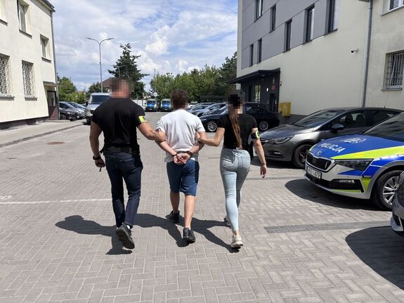nieumundurowani policjanci prowadzący zatrzymanego męzczyznę