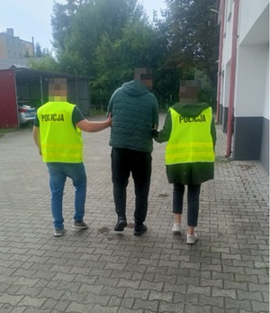 nieumundurowani policjanci w kamizelkach z napisem Policja prowadzą zatrzymanego mężczyznę