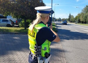 umundurowana policjantka kontroluje prędkość mierząc ją urządzeniem do pomiaru prędkości