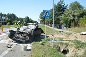 samochód na dachu leży na poboczu. Obok policjant wykonuje czynności
