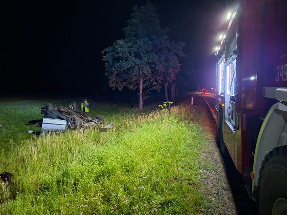 uszkodzony samochód na łące. Po prawej stronie zdjęcia widoczny fragment wozu strażackiego