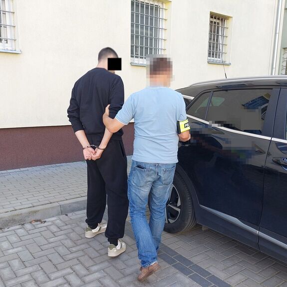 funkcjonariusz prowadzi zatrzymanego mężczyznę.