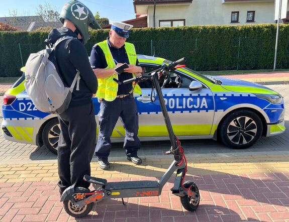 policjant umundurowany przy oznakowanym radiowozie i mężczyzna stojący przy hulajnodze elektrycznej