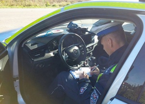 policjant siedzi w radiowozie i wypisuje dokumenty