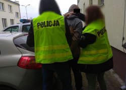 Zatrzymany mężczyzna prowadzony przez policjantów do radiowozu.