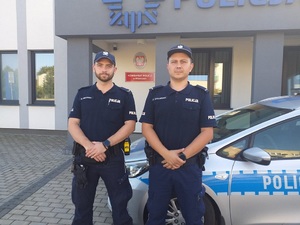 policjanci stojący przy radiowozie, w tle widać budynek komisariatu