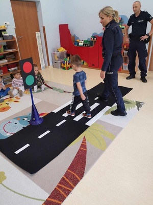 policjantka ćwiczy z dziećmi przechodzenie przez przejście dla pieszych