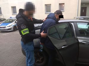 zatrzymany wsiada do radiowozu. Prowadzi go policjant kryminalny